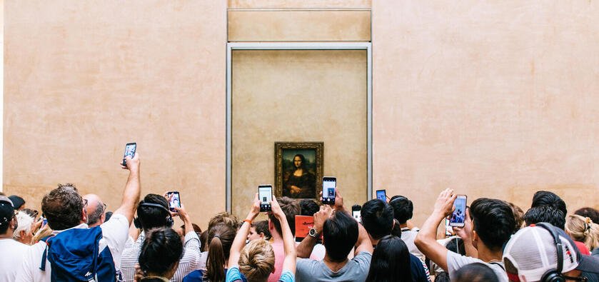 People standing in front of the Mona Lisa and taking pictures with their phones.