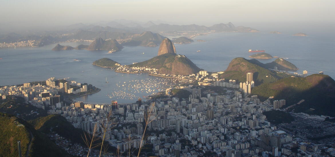 A photo overlooking Rio de Janeiro with buildings in a valley meeting a bay with mountains in the background.