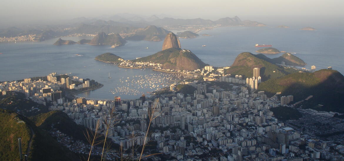 A photo overlooking Rio de Janeiro with buildings in a valley meeting a bay with mountains in the background.