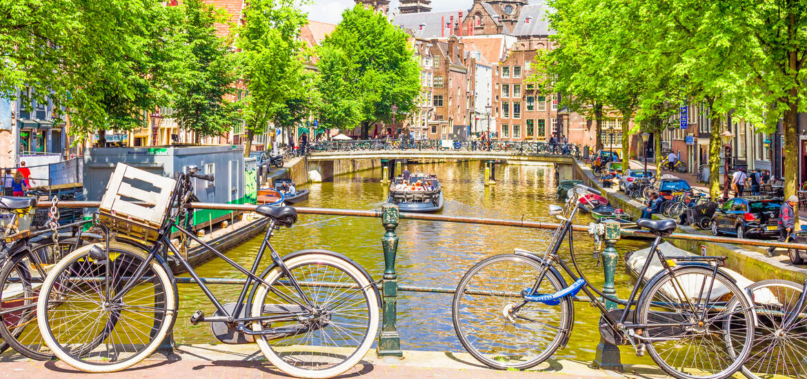 A view of an Amsterdam canal with bicycles parked on a bridge and a boat cruising below, surrounded by traditional Dutch buildings