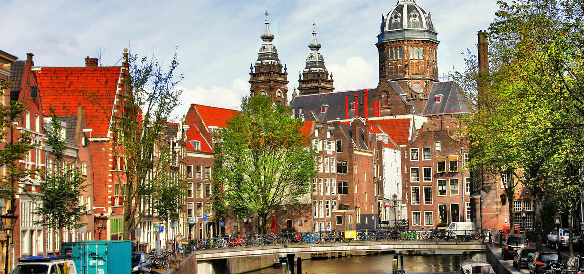 A scenic canal in Amsterdam with traditional Dutch houses, a historic church, and bicycles parked along the bridge in the background