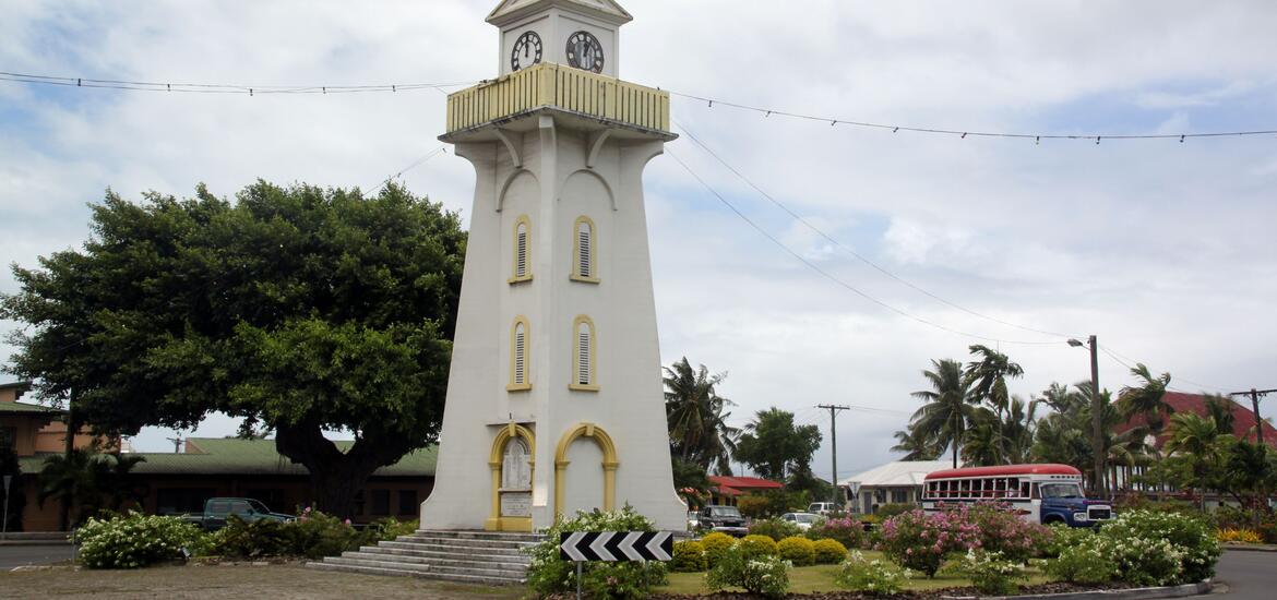 The iconic clock tower in the center of a square in Apia, Western Samoa, with palm trees and buildings in the background