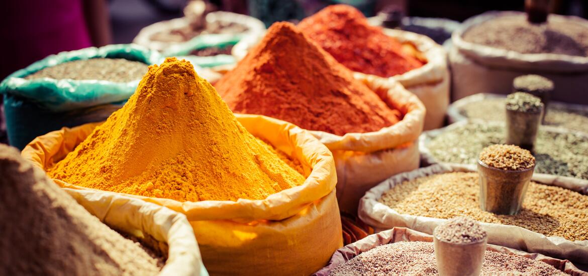 Vibrant piles of colorful spices, including bright orange and red powders, displayed in sacks at a local market in India