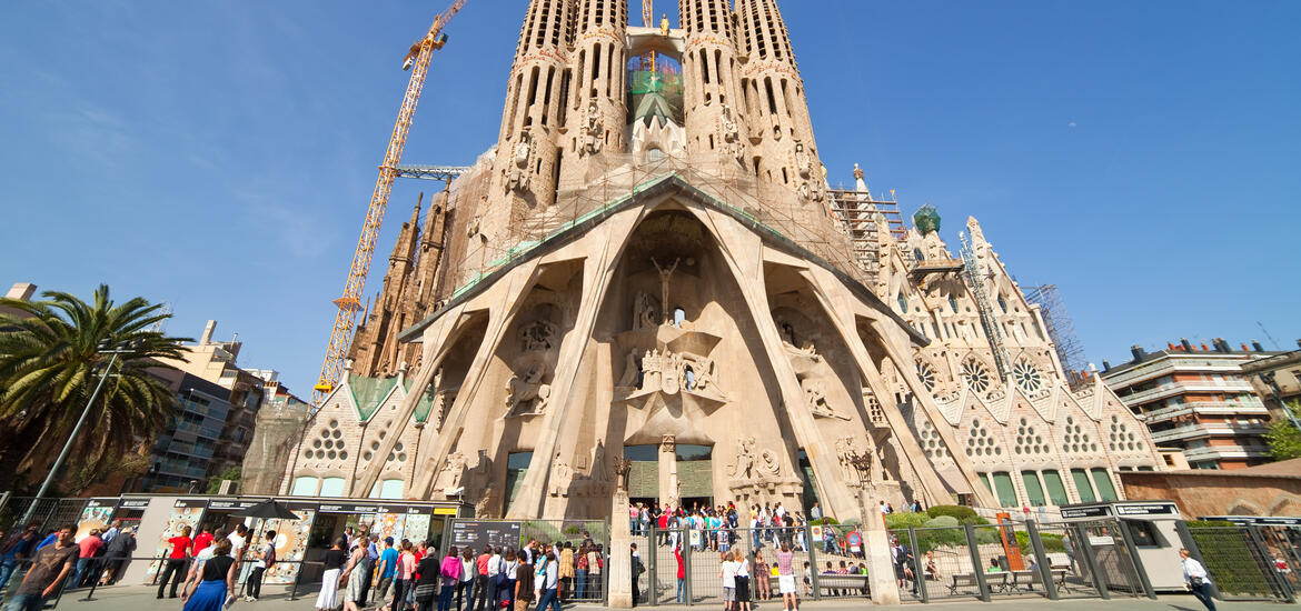 A view of La Sagrada Familia in Barcelona, showcasing its towering spires and intricate facade sculptures, with tourists gathering in front