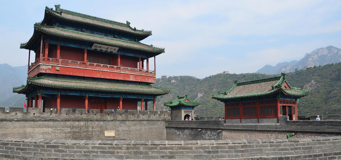 A traditional Chinese watchtower with green-tiled roofs and red walls at the Juyong Pass, part of the Great Wall of China, with mountainous terrain in the background