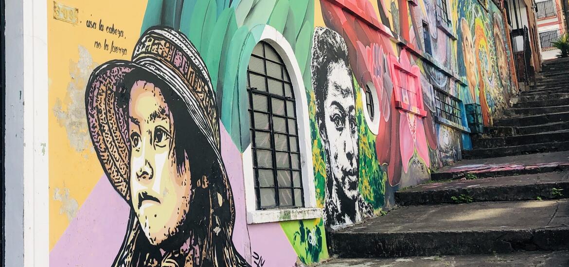 A mural showcasing colorful portraits and designs on the side of a building, next to a stone staircase in Cali, Colombia