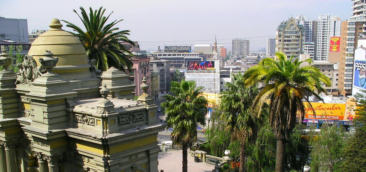 A view of historic buildings and palm trees in the foreground, with modern high-rises in the background in the city center of Santiago, Chile