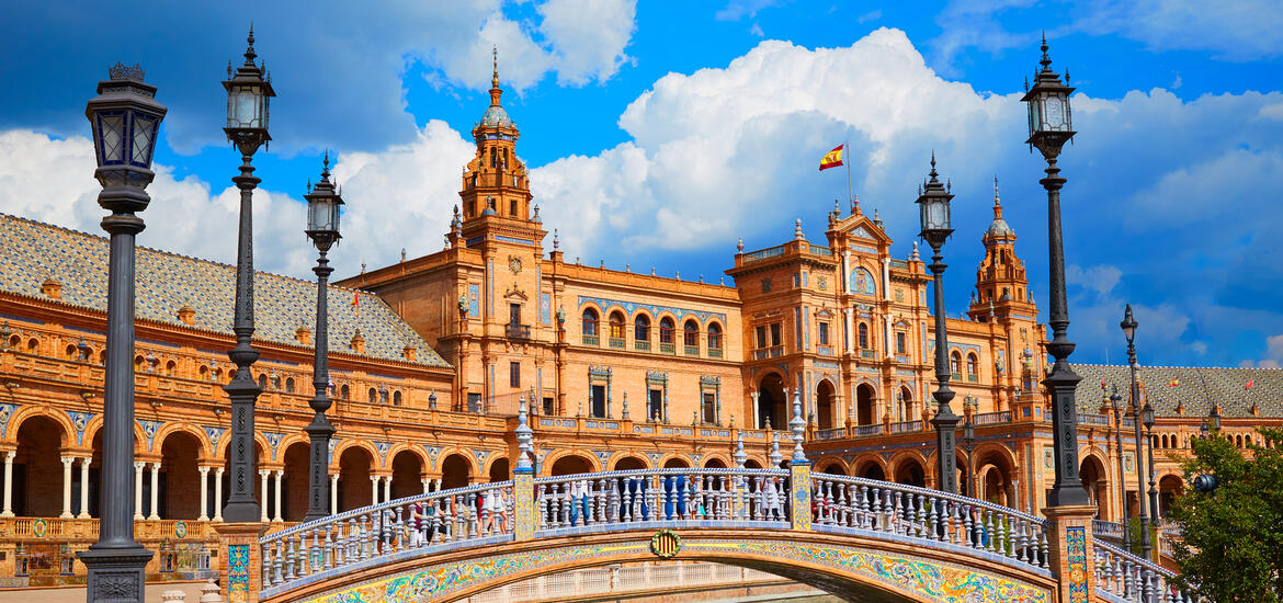 A view of Plaza de España in Seville, Spain, featuring ornate bridges over the canal, colorful ceramic details, and the grand Renaissance Revival building