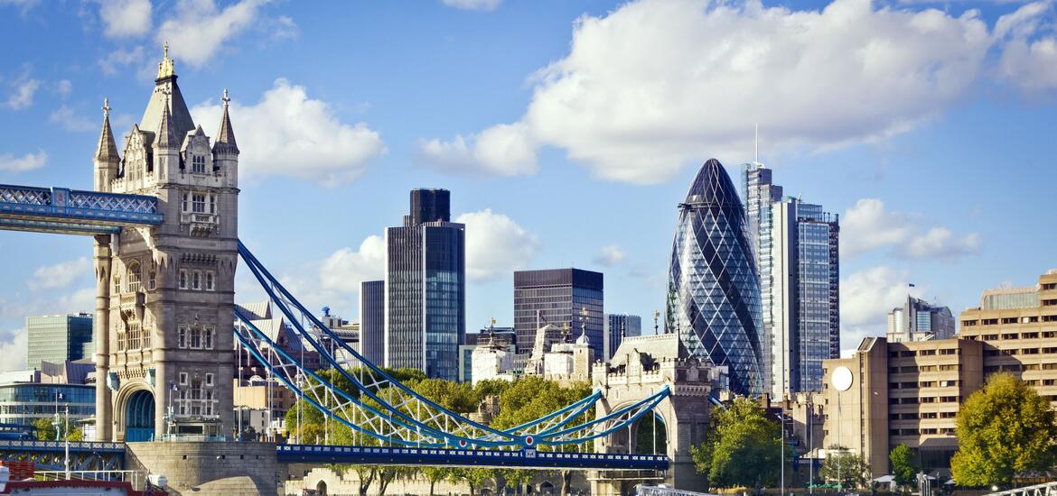 A view of London’s skyline featuring Tower Bridge, the Gherkin, and modern skyscrapers under a partly cloudy sky