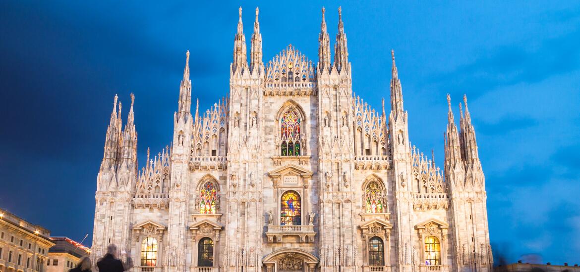 A view of Milan's gothic cathedral, Duomo di Milano, lit up at night with its intricate spires and stained-glass windows