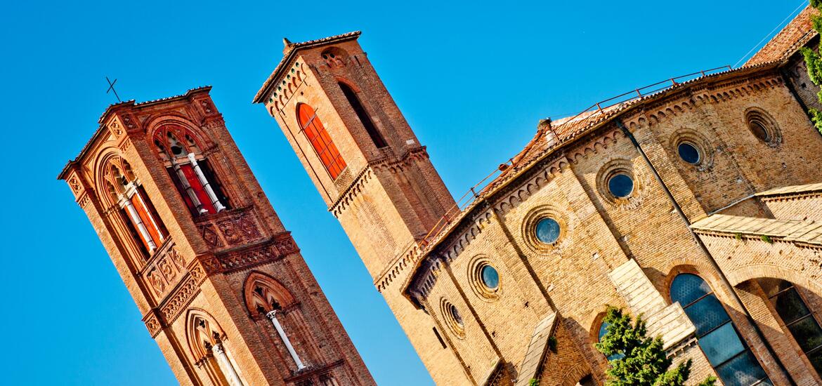 A close-up view of the Franciscan Church in Bologna, showcasing its tall brick towers and circular windows 