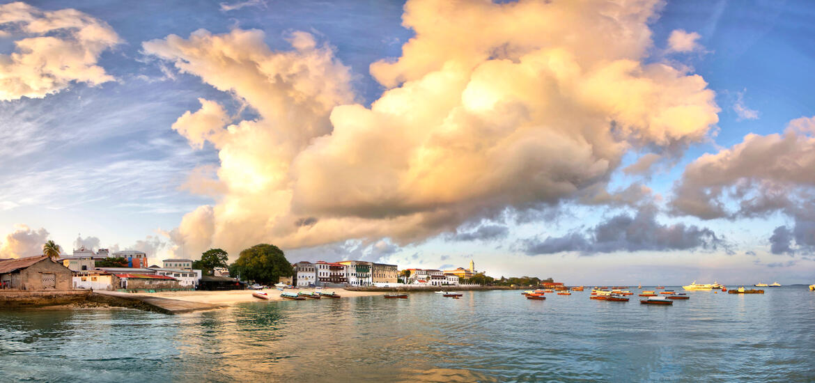 A panoramic view of Stone Town on Zanzibar Island, with boats floating on the calm water and vibrant buildings along the shoreline