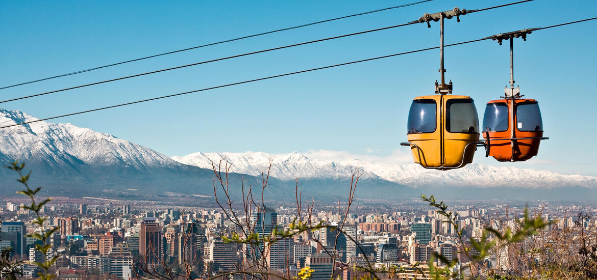 Yellow and orange cable cars suspended over the city of Santiago, with the snow-capped Andes Mountains in the background 