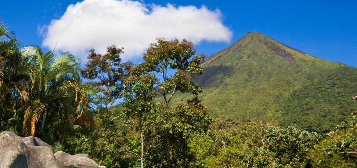 A view of the green hillsides and tropical vegetation surrounding the towering Arenal Volcano in Costa Rica.