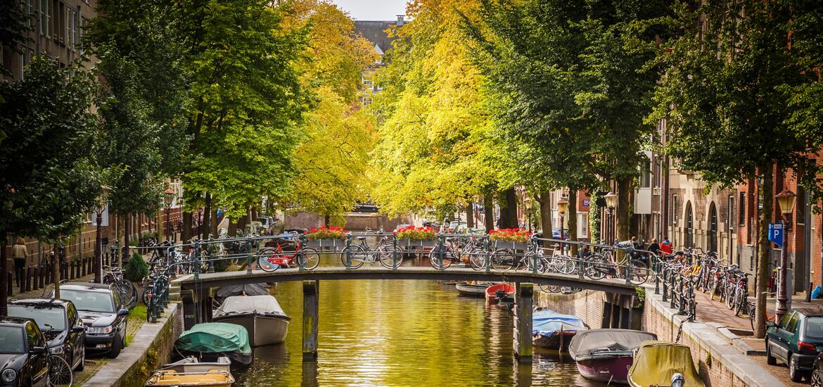 A scenic canal in Amsterdam lined with trees, bicycles parked on a bridge, and boats moored along the water