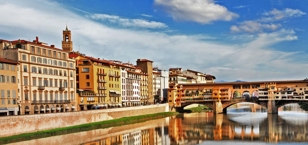 A view of the historic Ponte Vecchio bridge over the Arno River in Florence, Italy, with colorful buildings along the riverbank