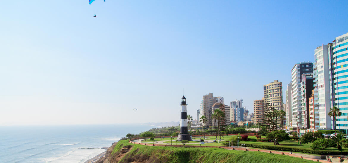 A view of the Miraflores district in Lima, Peru, featuring a lighthouse, tall buildings, and a paraglider over the coastline