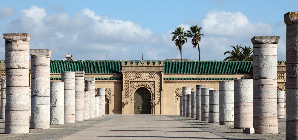 The Mausoleum of Mohammed V in Rabat, Morocco, featuring its ornate green-tiled roof and surrounded by stone columns, with palm trees in the background