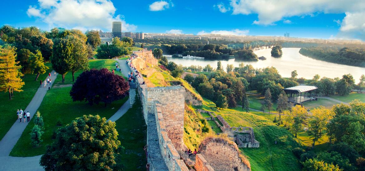 A scenic panorama of New Belgrade, with lush greenery, the river, and historical walls viewed from the Belgrade Fortress