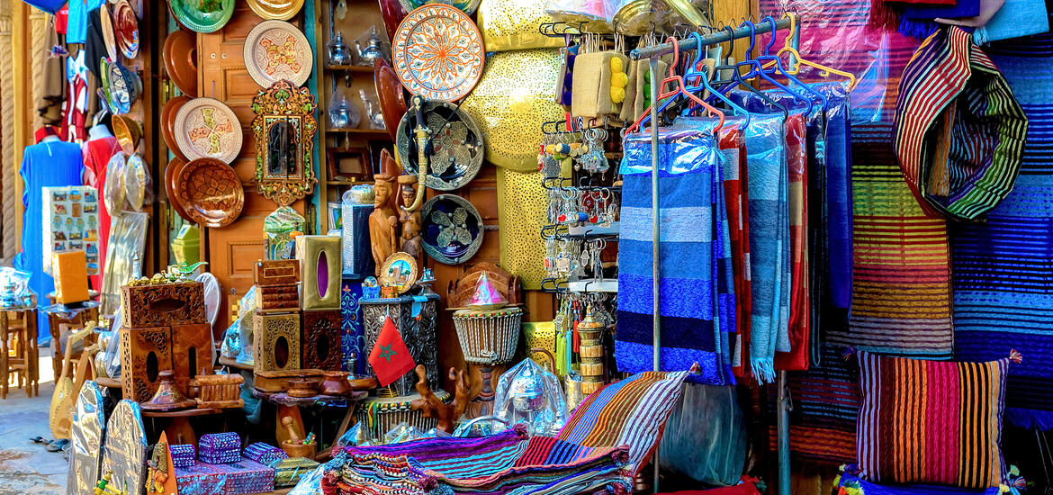 A vibrant market stall in a bazaar in Rabat, Morocco, displaying colorful scarves, handcrafted plates, wooden carvings, and other souvenirs