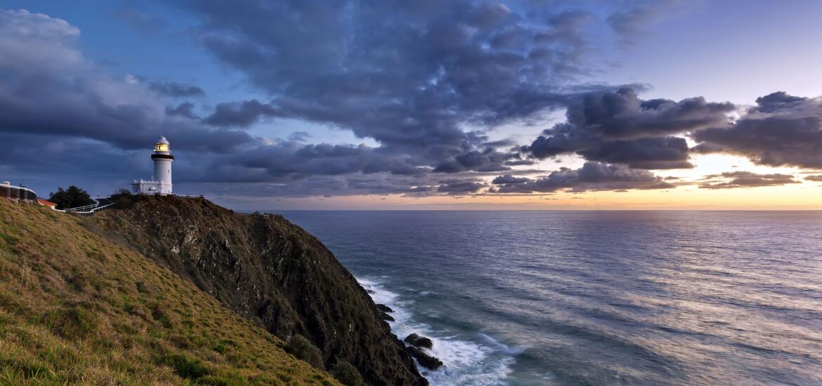View of the Cape Byron Lighthouse perched on a cliff, overlooking the ocean at sunrise
