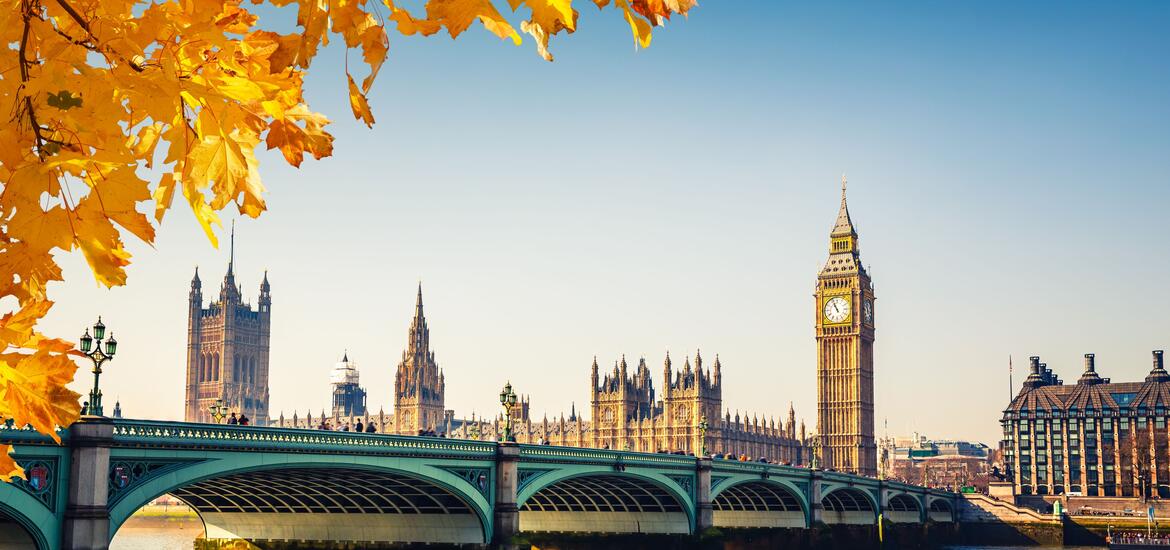Big Ben and the Houses of Parliament in London, framed by autumn leaves with Westminster Bridge in the foreground