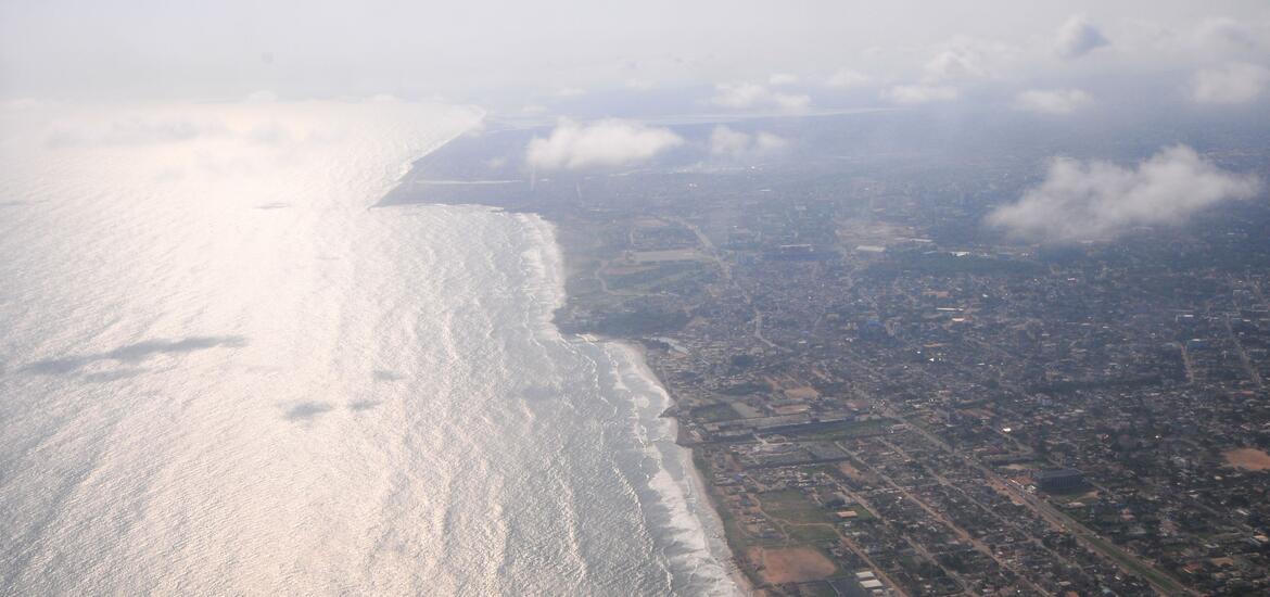 An aerial view of Accra, Ghana, showing the coastline and the urban landscape stretching along the shoreline