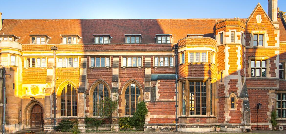 Pembroke College building in Cambridge with red-brick facade, large arched windows, and sunlight casting warm shadows on the building