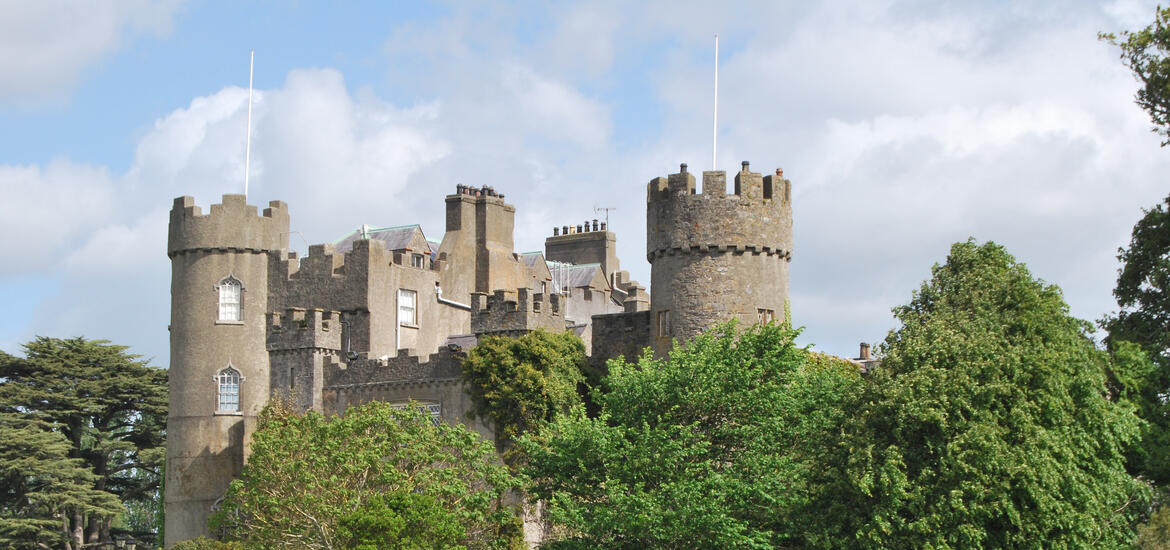 A view of Malahide Castle, a medieval fortress with rounded towers, surrounded by greenery in Malahide Demesne Regional Park near Dublin, Ireland