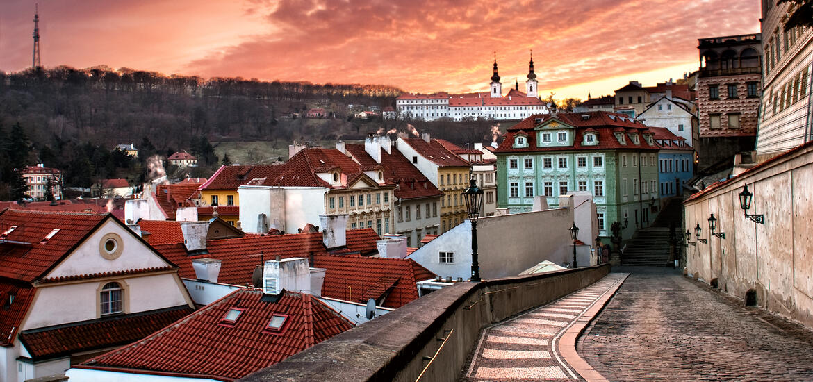 A view of Prague's red-roofed buildings and narrow streets, with a hillside and historic church in the background