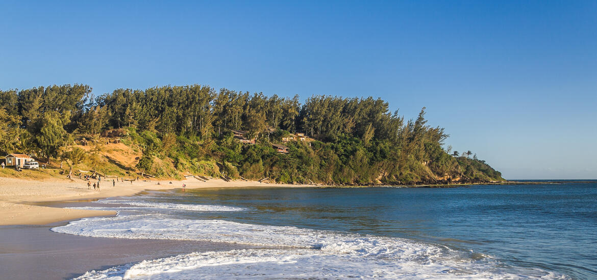 A view of Libanona Beach in Fort Dauphin, Madagascar, with waves crashing onto the sandy shore, backed by lush green hills