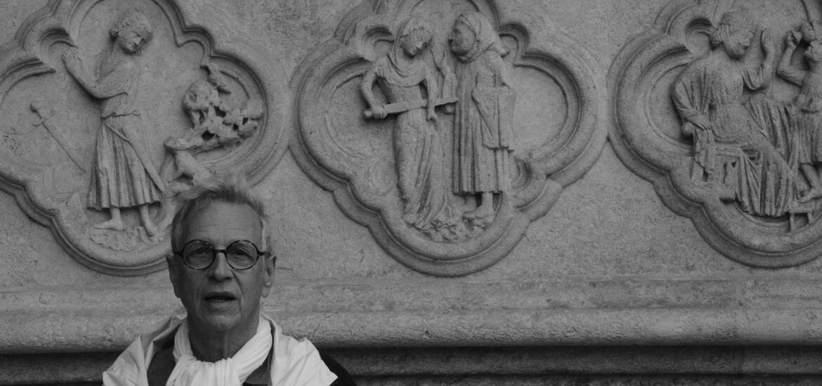 A person stands in front of detailed stone carvings depicting religious scenes on the wall of the Cathedral of Amiens