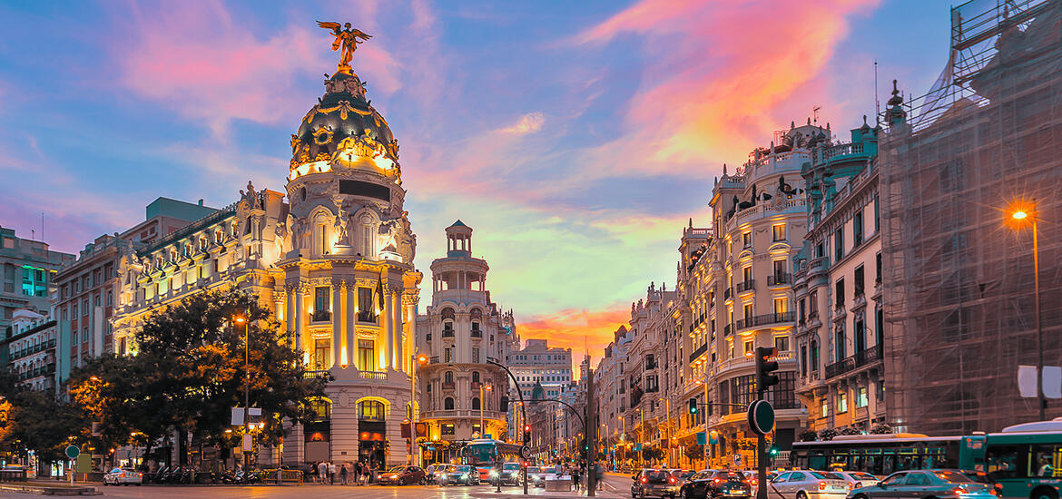 Evening view of Gran Vía in downtown Madrid, with the illuminated Metropolis building and surrounding architecture