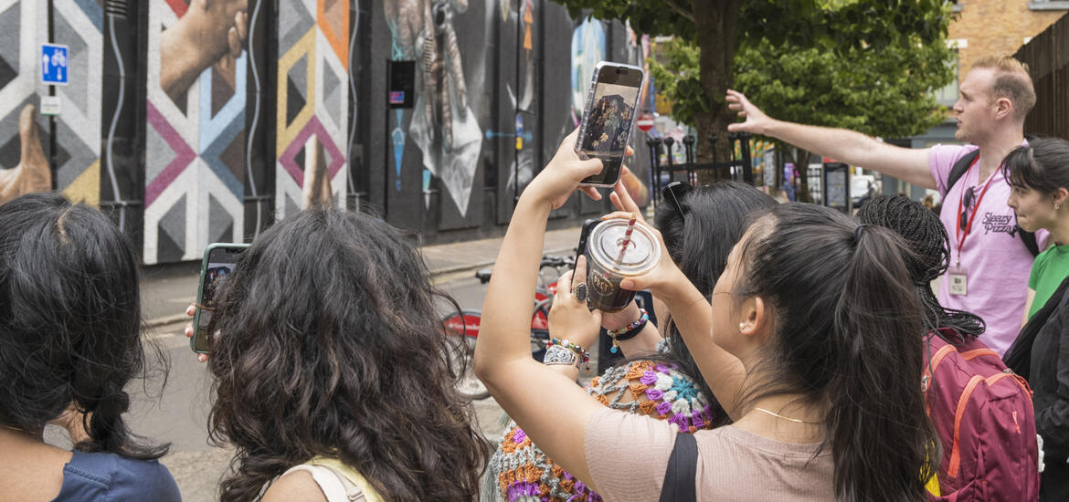 A group of students photographing vibrant street art in East London as a guide points out details