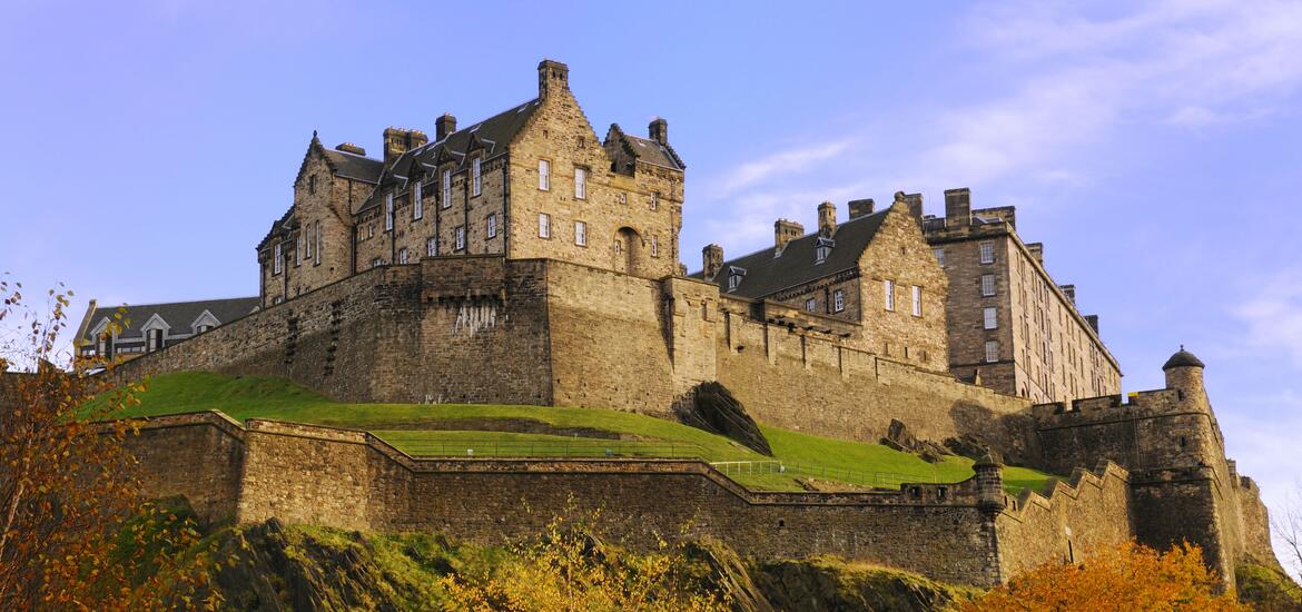 Historic Edinburgh Castle on a rocky hilltop, featuring medieval stone walls and turrets under a clear sky