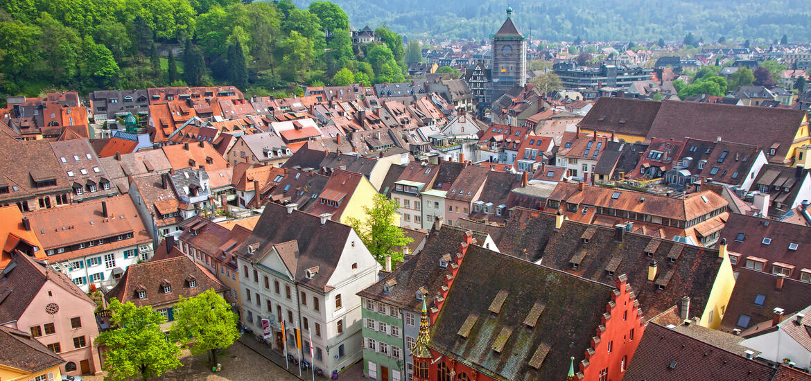 An aerial view of the vibrant red-tiled rooftops of Freiburg, Germany, with the historic clock tower and surrounding greenery in the background