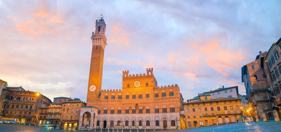  A sunset view of the Palazzo Pubblico in Siena, with its orange-brown facade and the tall Torre del Mangia clock tower