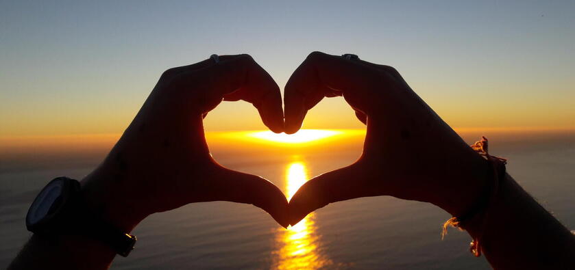 The silhouette of hands making a heart with an ocean sunset in the background