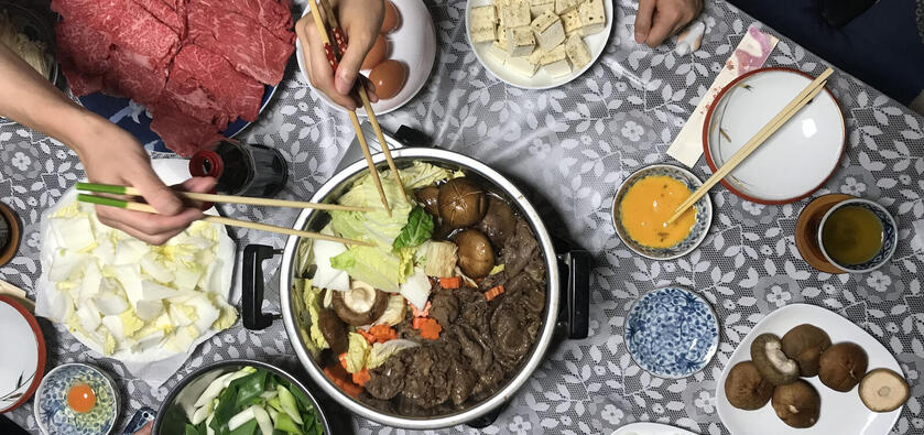 An aerial view of a traditional hotpot meal with people using chopsticks to eat