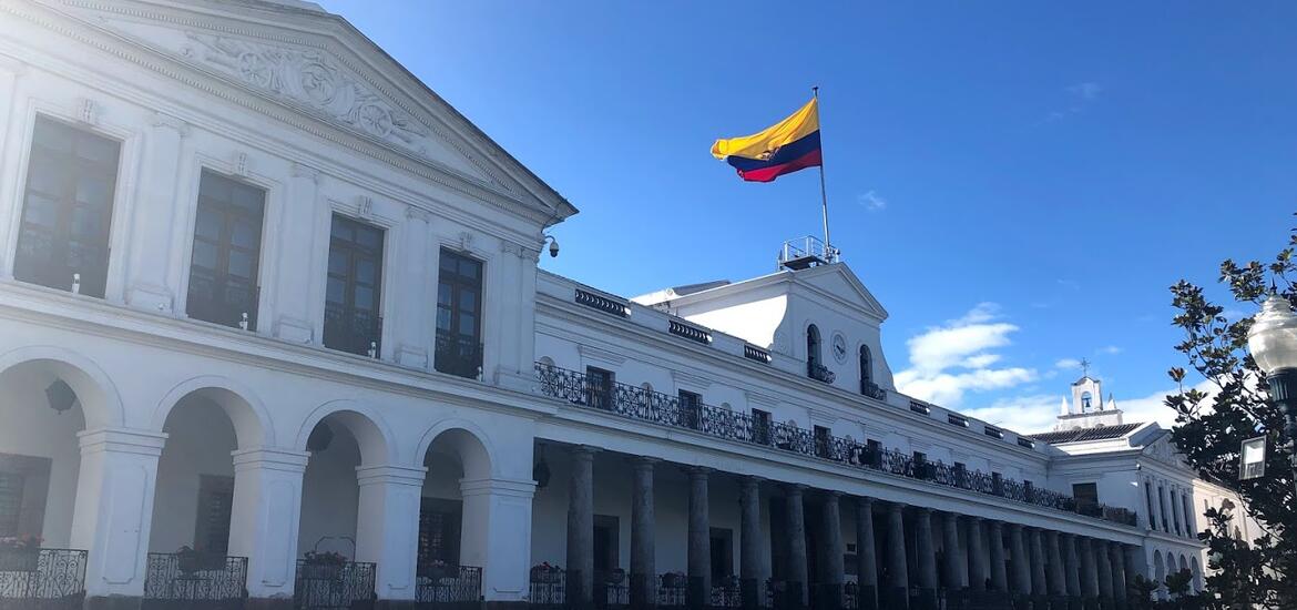 The Government Palace of Quito, a neoclassical white building with arched windows and columns, with the Ecuadorian flag flying on top