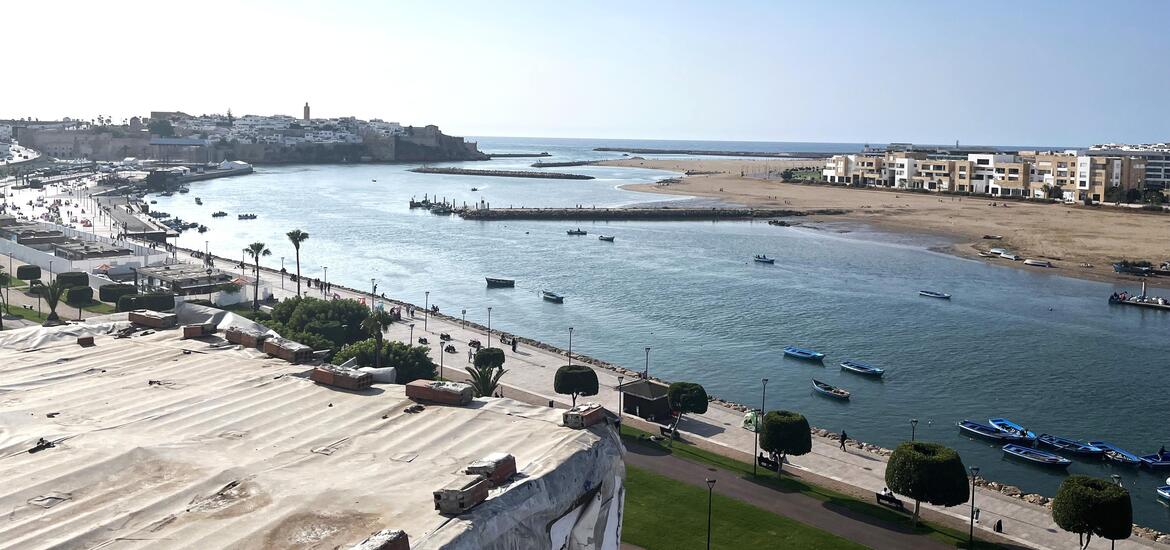 A view of the Bou Regreg river from the rooftop of a house in Rabat, Morocco, with boats on the water, a riverside promenade, and buildings lining the opposite shore