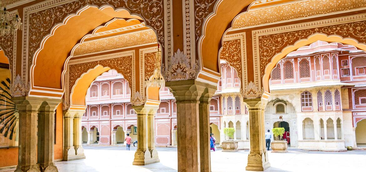 Ornate archways with intricate designs in shades of orange and gold at the Chandra Mahal in City Palace, Jaipur, India, with a view of the palace courtyard