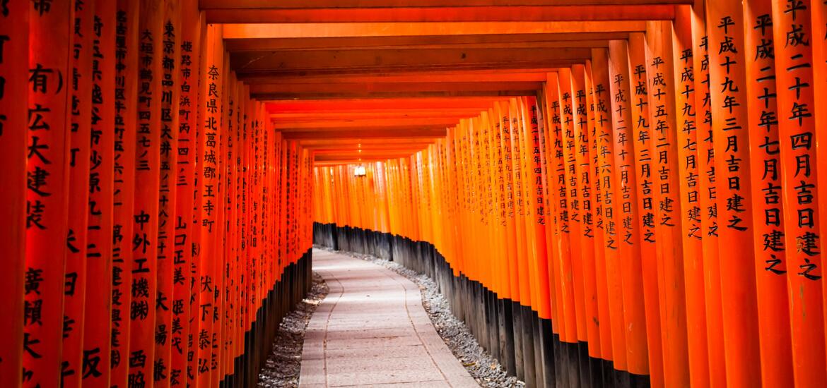 A pathway lined with vibrant red torii gates at Fushimi Inari-taisha Shrine in Kyoto, Japan, with Japanese inscriptions on each gate