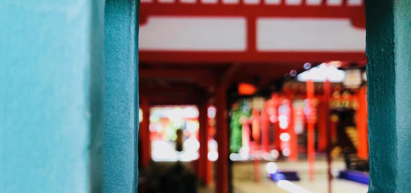Looking through a small square window on a turquoise wall into the blurry interior of a building in Japan