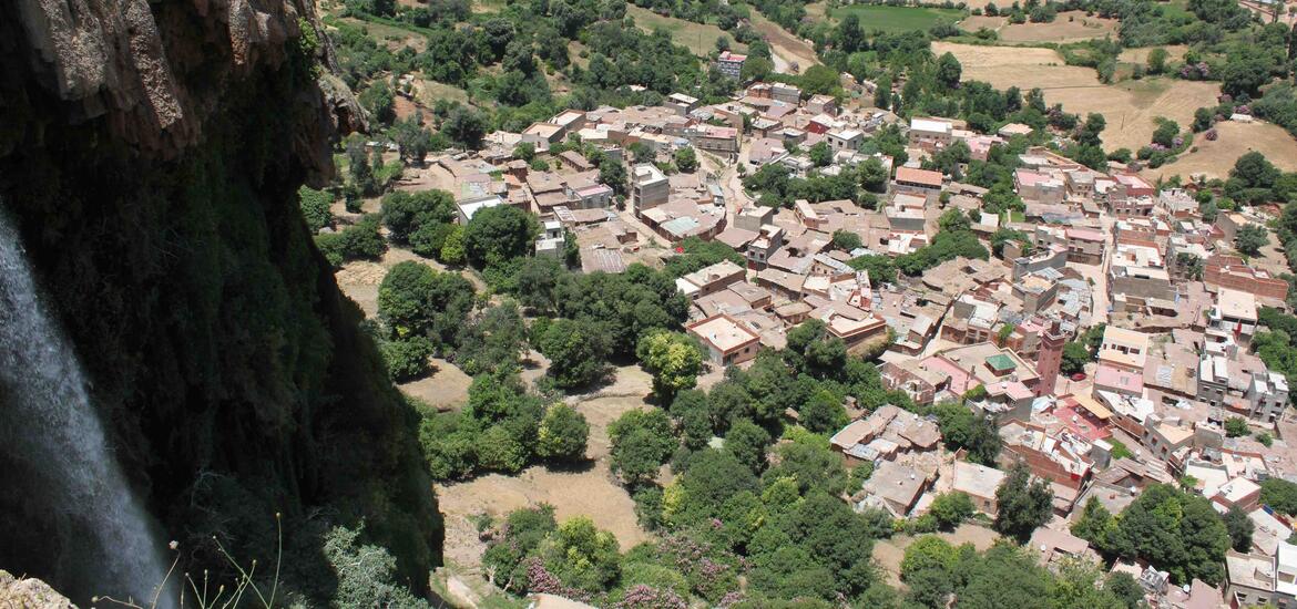 A scenic view of the Akchour Waterfall hike in Morocco, featuring clear green water flowing between rocky cliffs and lush greenery