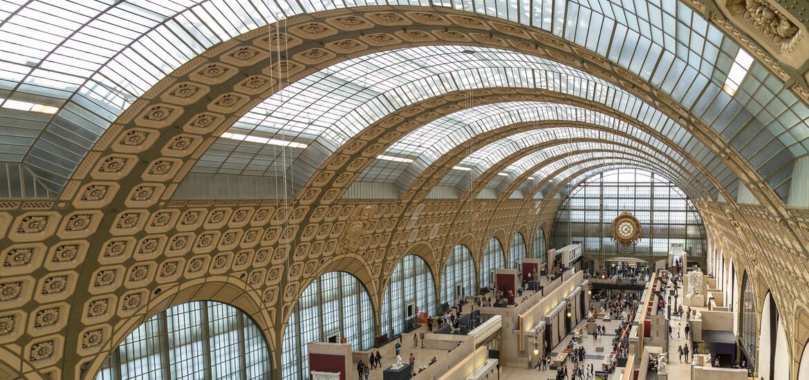 The grand gallery of the Musée d'Orsay in Paris, featuring a stunning arched glass ceiling and intricate architectural details, with visitors exploring the exhibits below