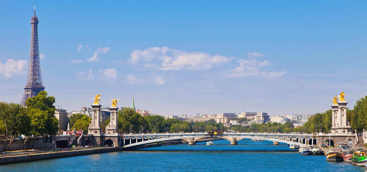 A view of the Eiffel Tower rising in the background and the ornate Pont Alexandre III bridge spanning the Seine River in Paris