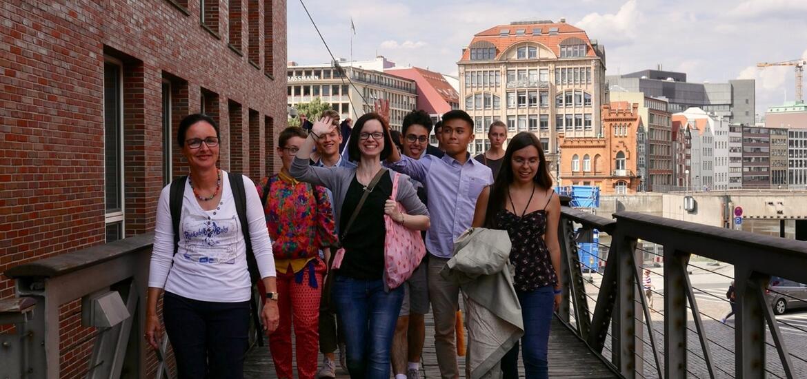 A group of smiling students stands outside in front of a bridge and a river
