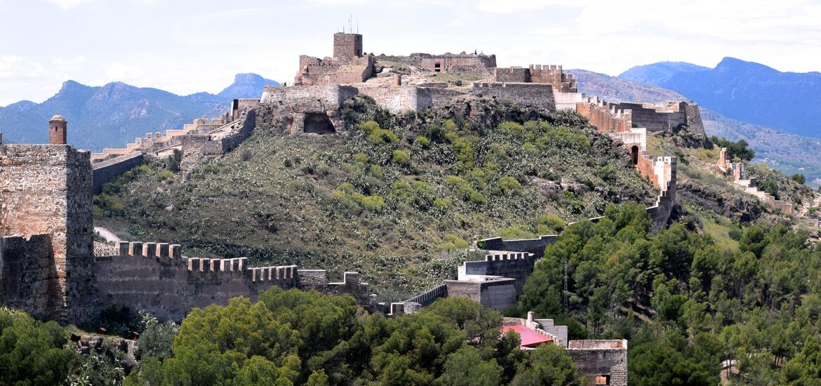 The stone ruins of a castle stand on a hilltop surrounded by mountains.