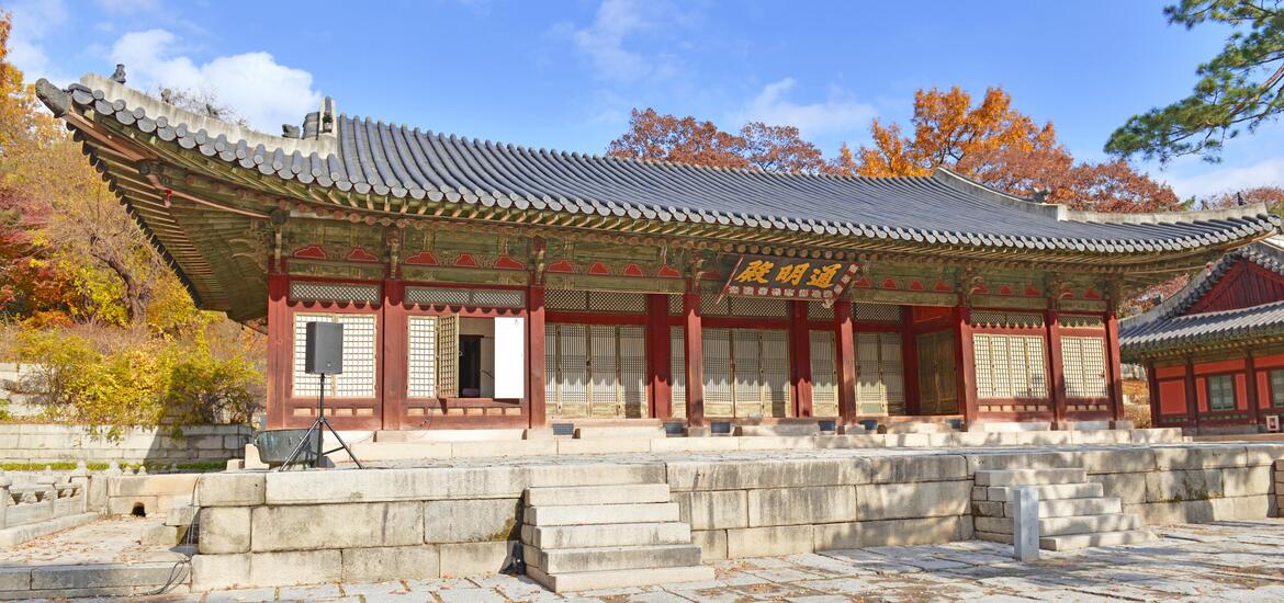 A view of the historic Changgyeonggung Palace in Seoul, showcasing its traditional Korean architecture with curved tiled roofs, surrounded by colorful autumn trees